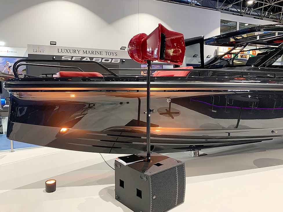 Void Acoustics Arcline 118 Subwoofer und rotes Hornlautsprechersystem auf einer Messe, platziert vor einem luxuriösen schwarzen Boot