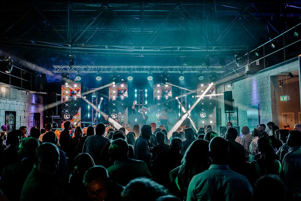 Menschen vor einer Bühne mit Band, Moving Heads, LED-Wandstreifen, Traversen und LED-PAR-Scheinwerfern
